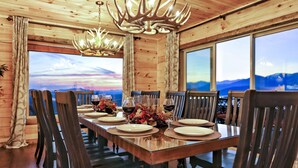 A wooden dining room with a large table set for six, surrounded by chairs, and a chandelier with antler-like light fixtures.