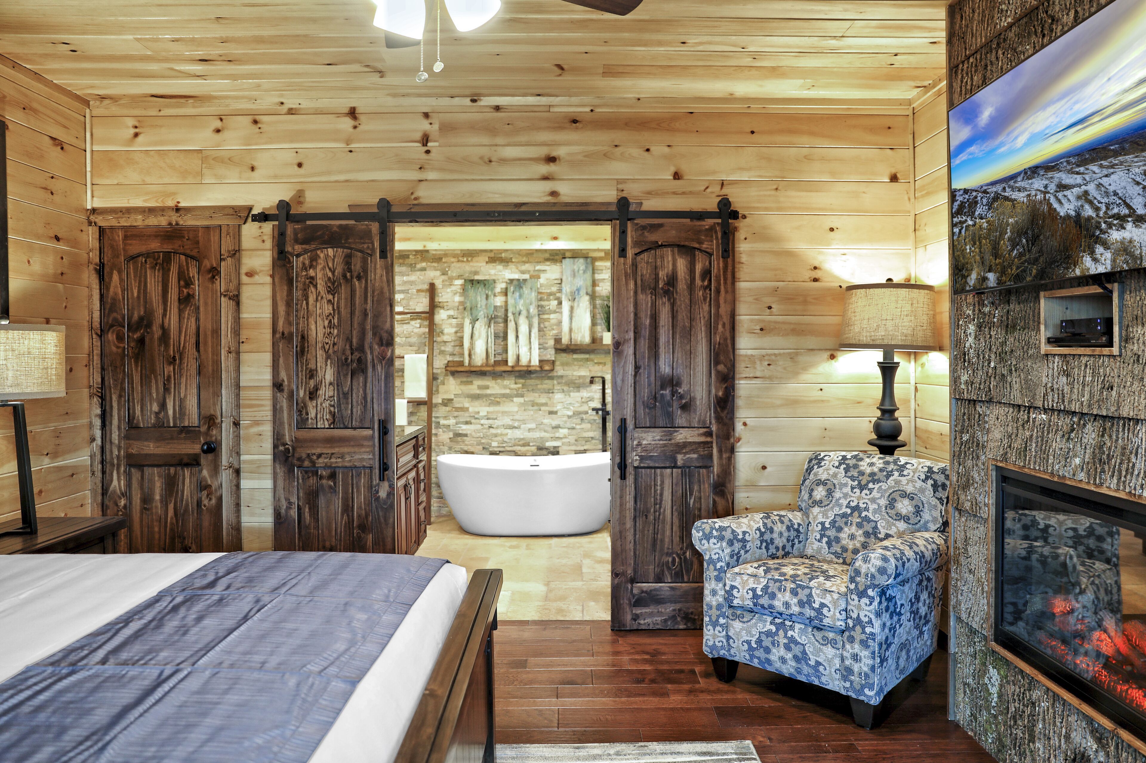Ein Schlafzimmer einer Holzhütte mit einem Bett, einem Sessel, einer Badewanne und einem Kamin.