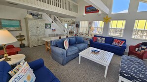 A spacious living room with blue sofas, a white coffee table, and a staircase leading to an upper level. - enJoy | gulfside, great price, open starting 8/8 (Dauphin Island)