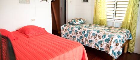 A bedroom with two beds, one with a red bedspread and the other with a patterned bedspread. There is a window with yellow curtains, a starfish decoration on the wall, and a butterfly decoration.
