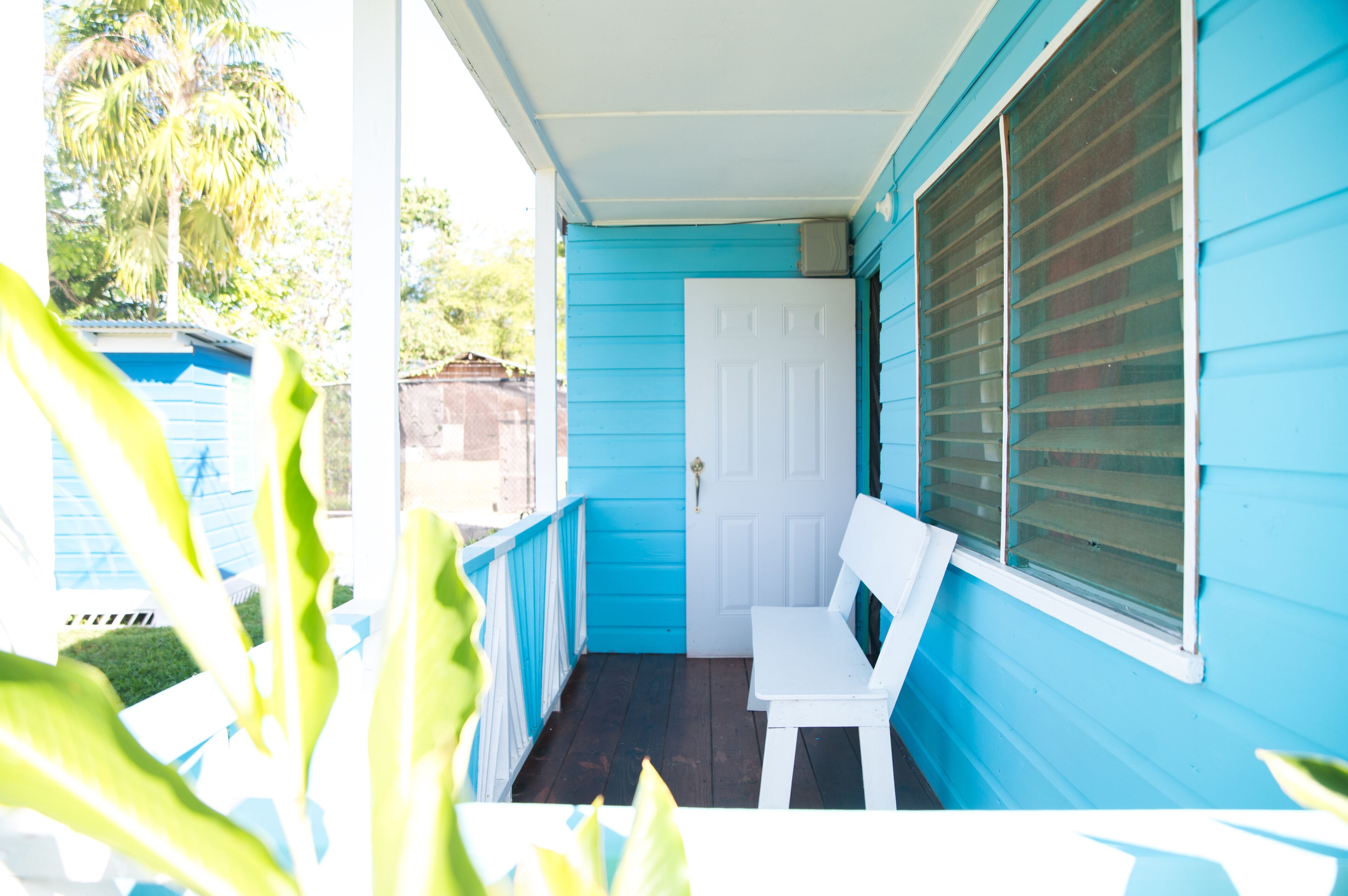 A porch with a white bench, a door, and a window with blinds.