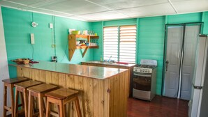 A kitchen with a wooden bar stool area, a stove, and a refrigerator. - Cali Cottages (Negril)