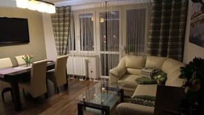 A modern living room with a glass coffee table, beige sofa, and a dining area with a table and chairs. - Torun Apartment Modern apartment in the Torun city center (Jakubskie Przedmiescie)