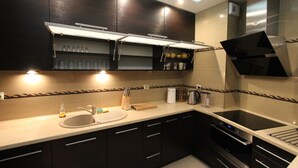 A modern kitchen with dark cabinetry, a built-in oven, a sink, and a countertop with various kitchen items. - Torun Apartment Modern apartment in the Torun city center (Jakubskie Przedmiescie)