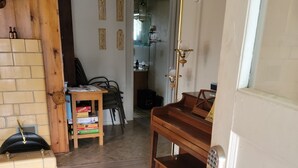 Una habitación con piso de madera, un piano, una puerta con cerradura electrónica y una silla con una caja de libros.