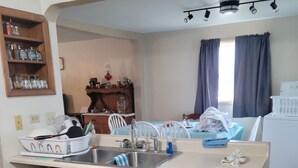 Una cocina compacta con fregadero, armarios de madera, un pequeño comedor y una ventana con cortinas.