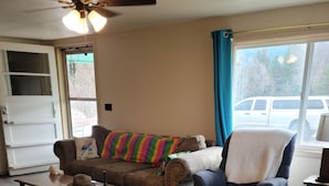 Una sala de estar con un sofá marrón, un sillón azul, una mesa de centro de madera y una alfombra estampada.