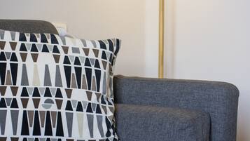 Un salon moderne avec un canapé gris, des coussins à motifs, une lampe sur pied et une petite plante posée sur une table en bois.