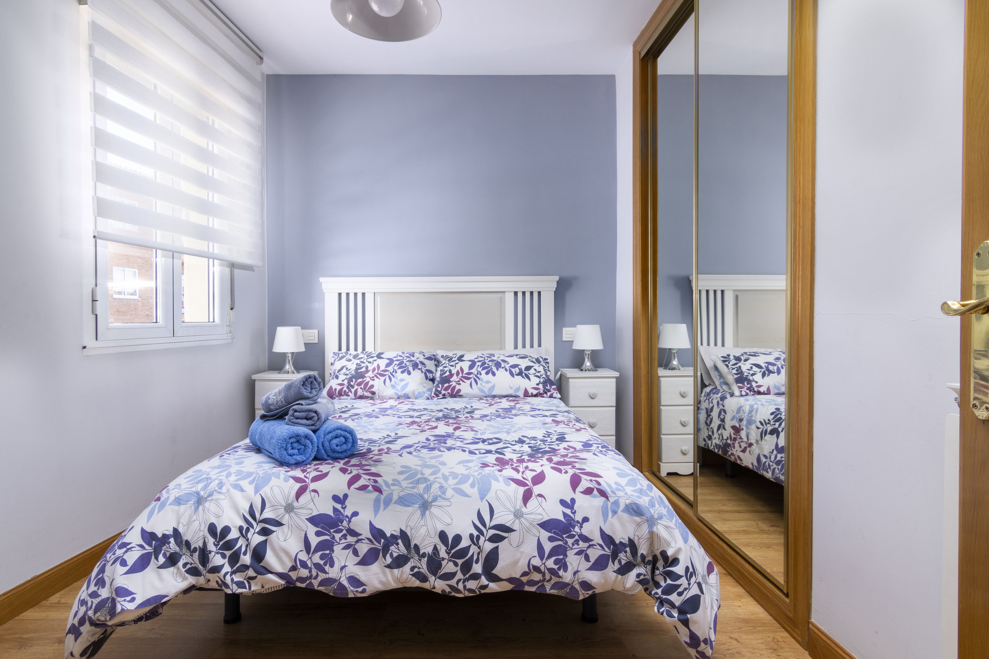 Un dormitorio con cama, mesitas de noche, un espejo y una ventana con persianas.
