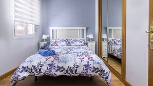 A bedroom with a bed, bedside tables, a mirror, and a window with blinds.