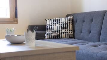A living room with a grey sofa, a patterned pillow, a small plant, and a bowl on a wooden table.
