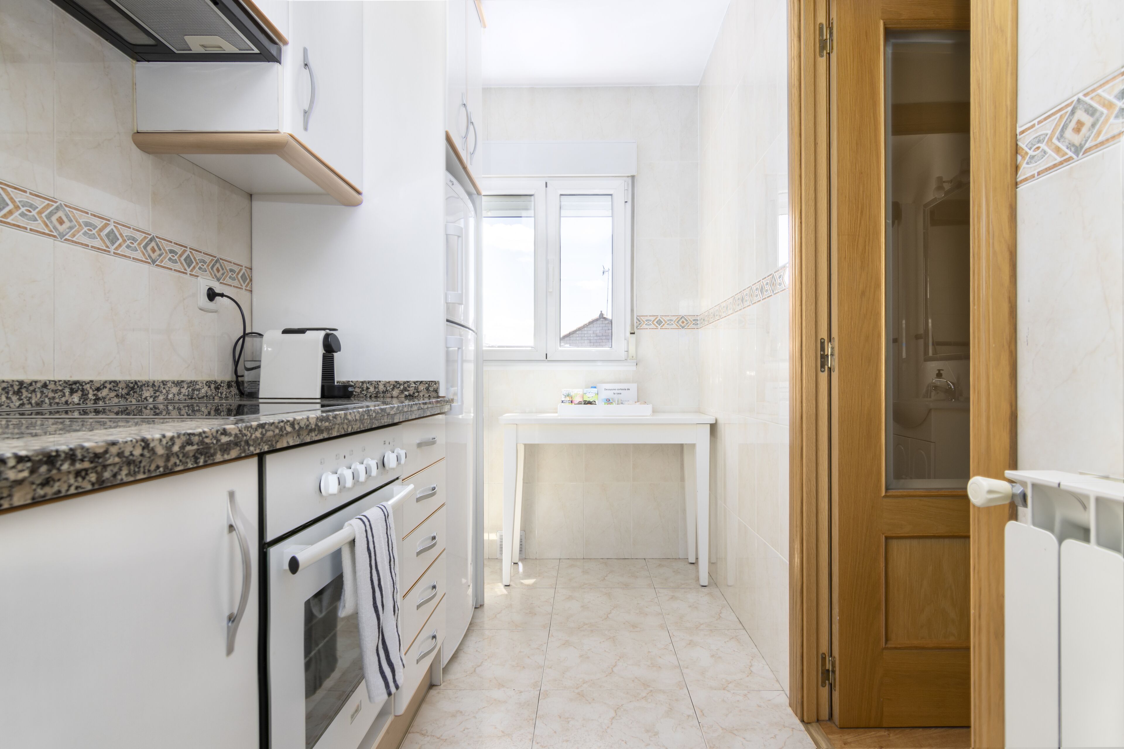 Una cocina estrecha con horno empotrado, una encimera con cafetera y una ventana sobre el fregadero.