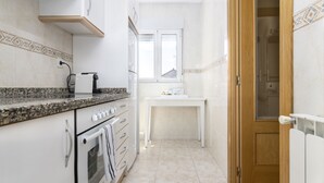A narrow kitchen with a built-in oven, a countertop with a coffee maker, and a window above the sink.
