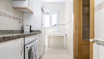 Una cocina estrecha con horno empotrado, una encimera con cafetera y una ventana sobre el fregadero.