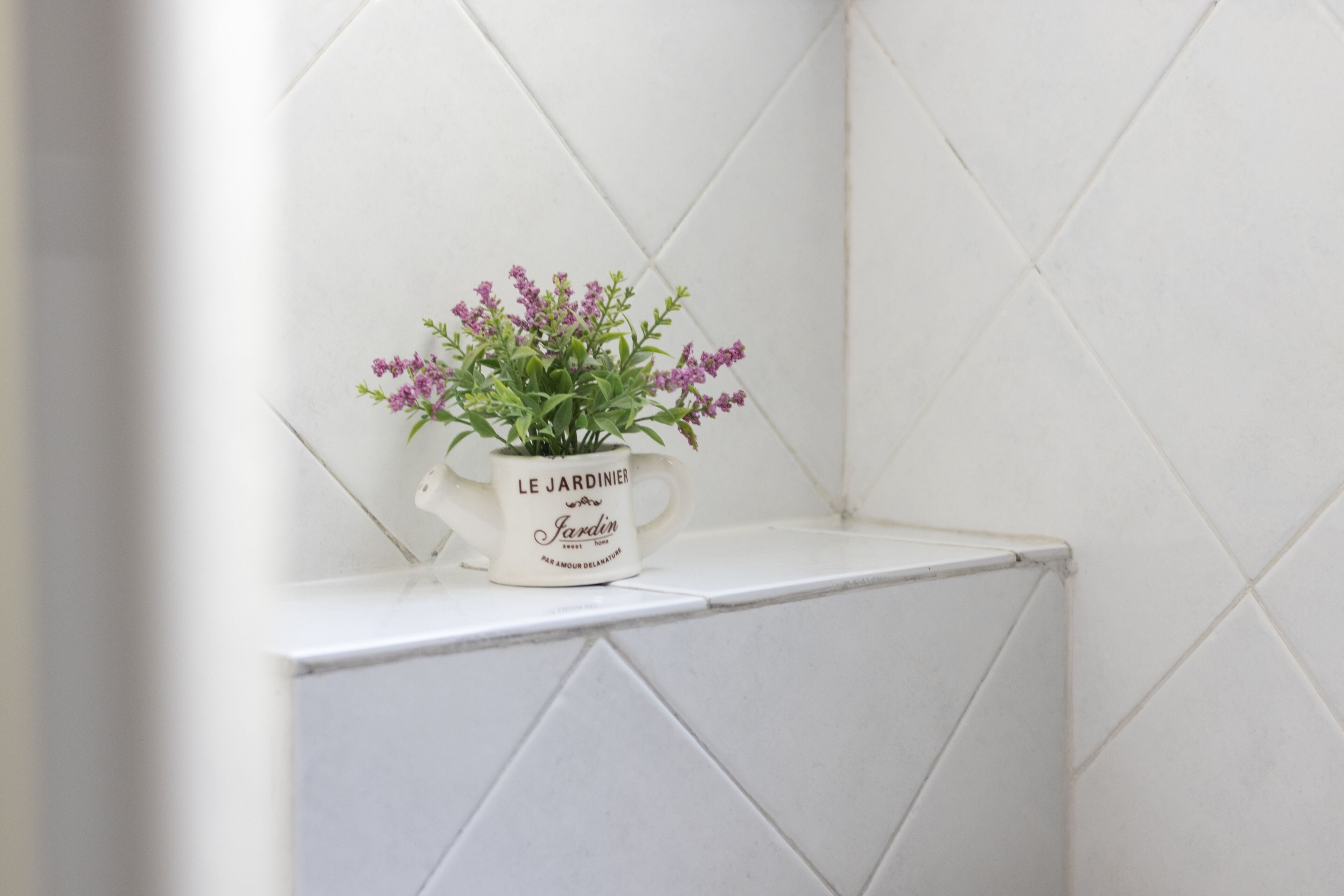 A white ceramic pot with text on it, placed on a white tiled ledge.