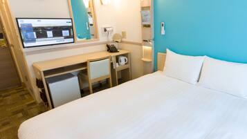 A hotel room with a bed, a desk, a computer, a mirror, and a clock on the wall.