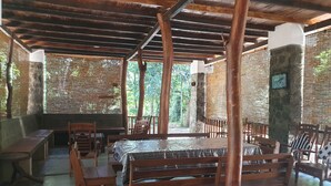 An outdoor dining area with wooden tables and benches, surrounded by stone pillars and covered by a wooden roof. - Jungle House Udawalawe Holiday Lodge (Udawalawa)