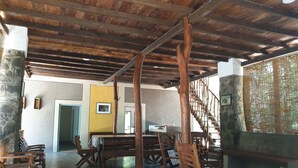 A spacious room with a high ceiling, wooden beams, and a stone wall. There are several wooden chairs and a table, and a staircase is visible in the background. - Jungle House Udawalawe Holiday Lodge (Udawalawa)