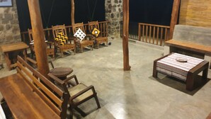 A rustic outdoor seating area with wooden furniture and a stone wall backdrop. - Jungle House Udawalawe Holiday Lodge (Udawalawa)