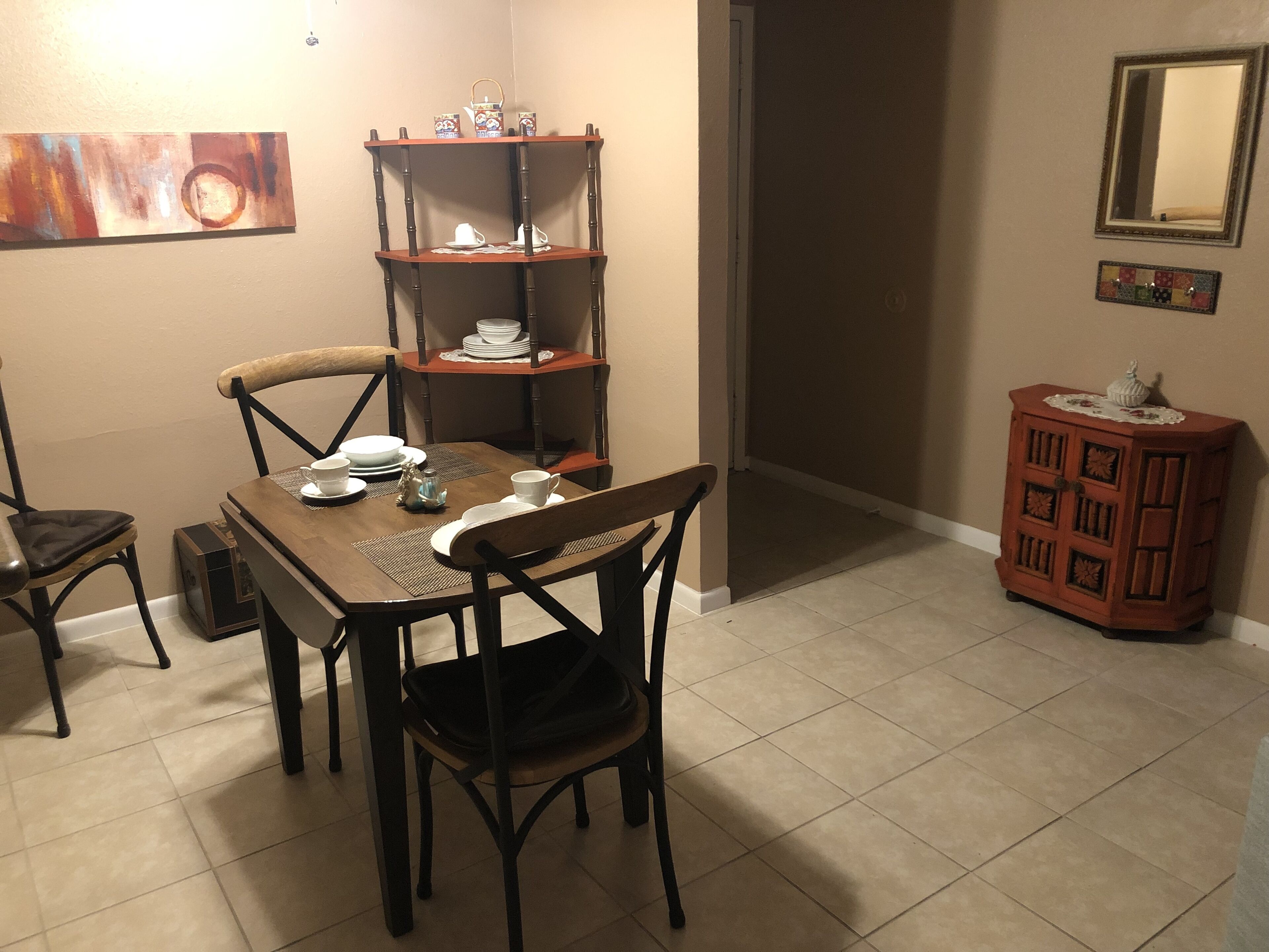 Een eethoek met een houten tafel voor vier personen, omringd door stoelen. Een houten kast met decoratieve objecten staat aan de rechterkant.