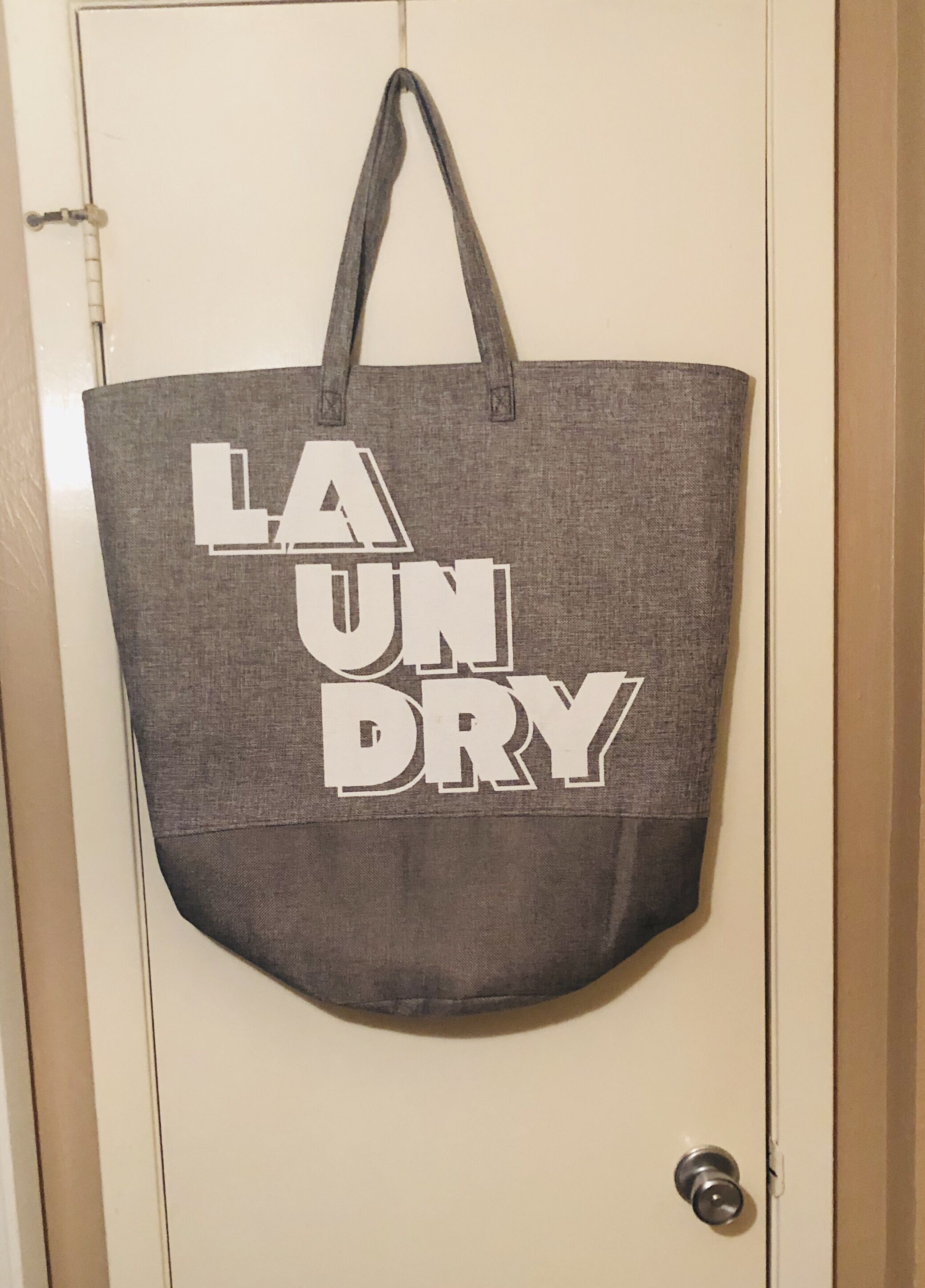 Een grijze tas met de tekst 'LAUNDRY' hangt aan een deur.