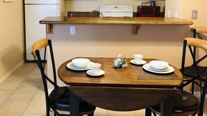 A compact kitchen with wooden cabinets, a white refrigerator, a microwave, and a stove. There is a dining table with four chairs and a small decorative item on the table. - Seaside Villa by the Oso Bay Comfortable Bed! (Corpus Christi)