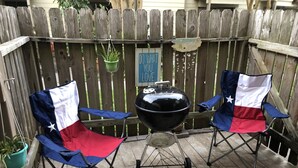 Two Texas state flags on folding chairs, a black grill, and a wooden fence with a 'Do What You Love' sign. - Seaside Villa by the Oso Bay Comfortable Bed! (Corpus Christi)