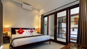 A hotel room with a large bed, a glass door leading to a balcony, and a small table with a vase. - Magical Estate, Walk to Seminyak Beach (Seminyak)
