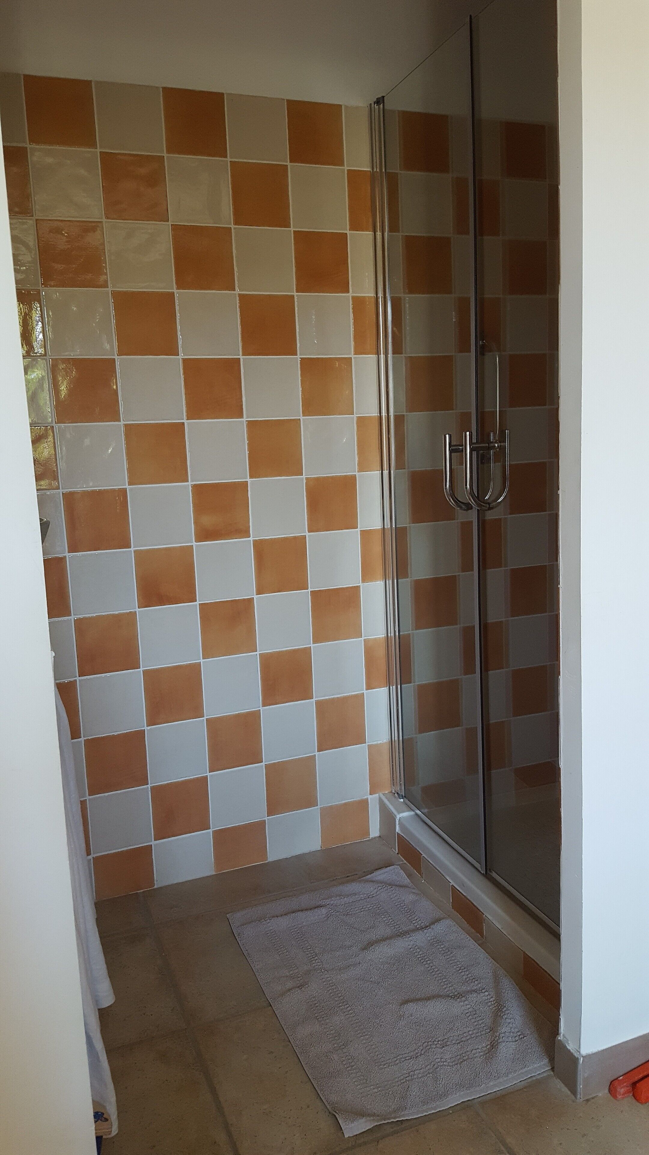 Een badkamer met een betegelde muur, een glazen douchecabine en een witte handdoek op de vloer.