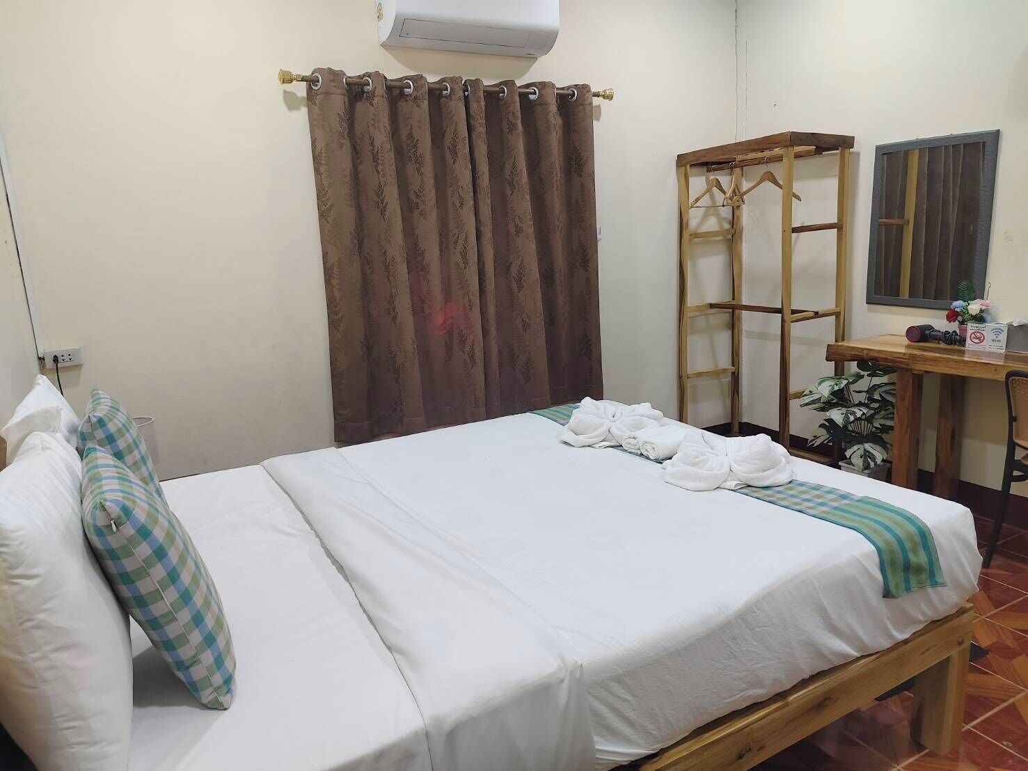 A neatly made bed with white linens, a wooden bedside table with a mirror, and a brown curtain.