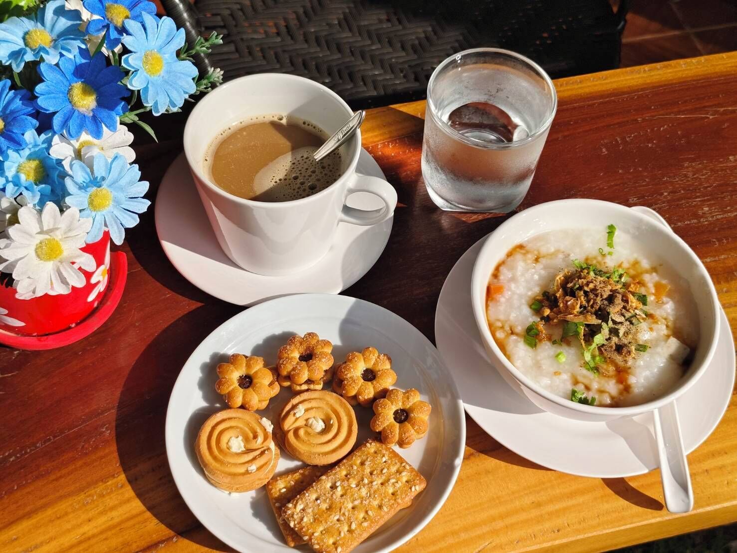 A table with a cup of coffee, a glass of water, a bowl of rice with toppings, and a plate of pastries.