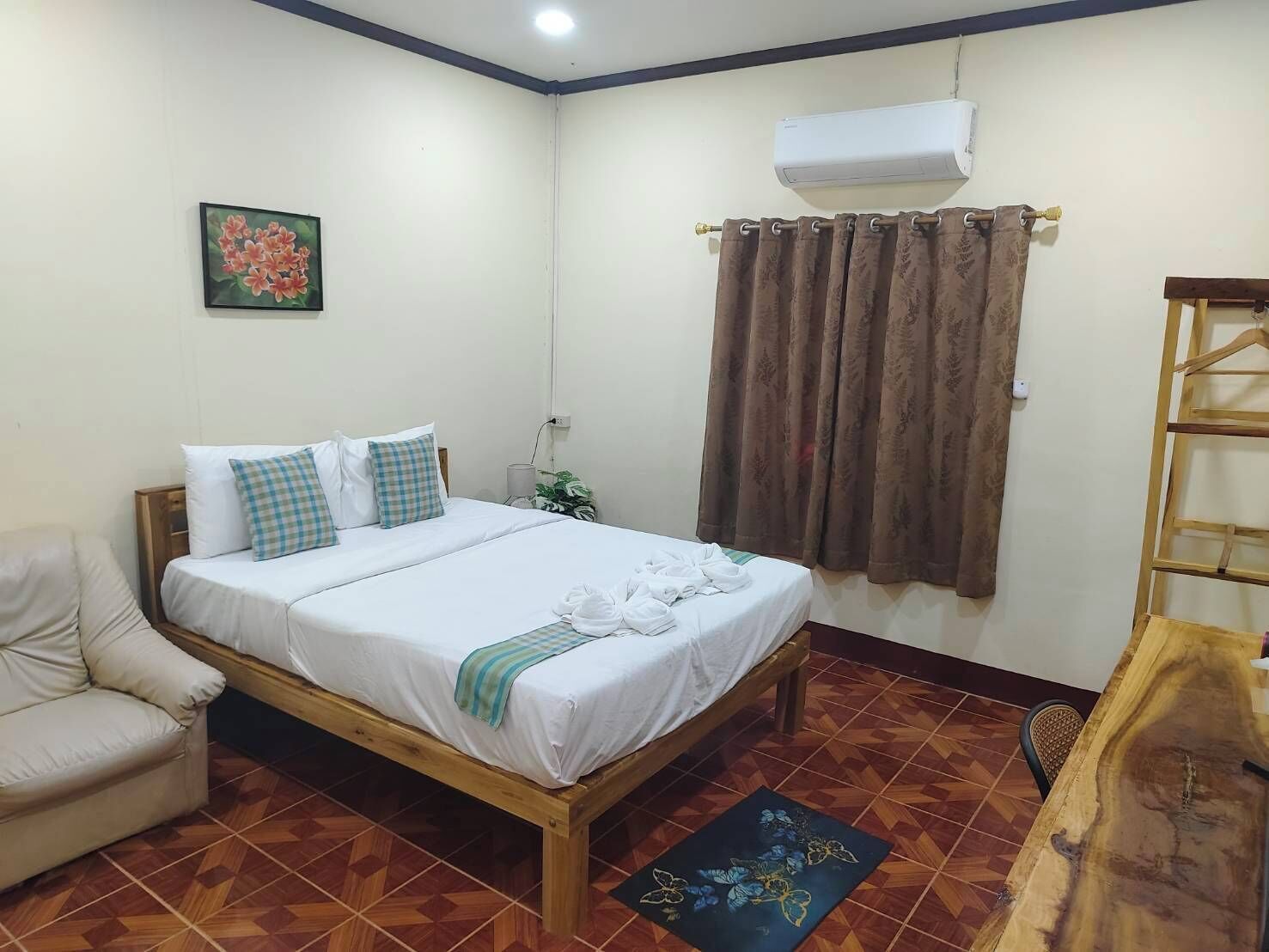 A hotel room with a bed, a chair, an air conditioning unit, and a curtain.