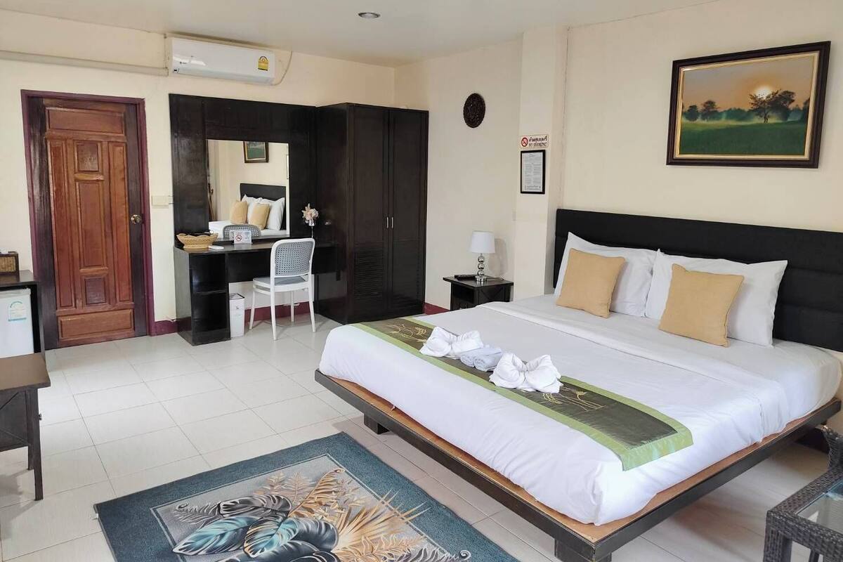 A hotel room with a bed, a desk, a chair, a wardrobe, and a painting on the wall.