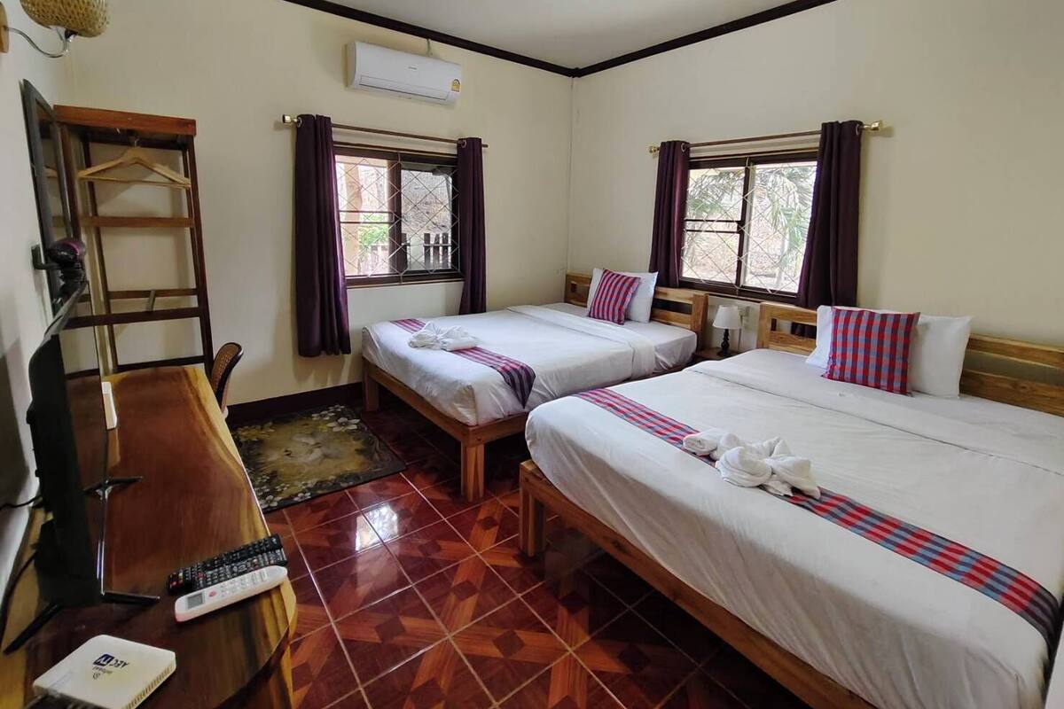 A hotel room with two beds, a desk, a chair, an air conditioner, and a window with curtains.