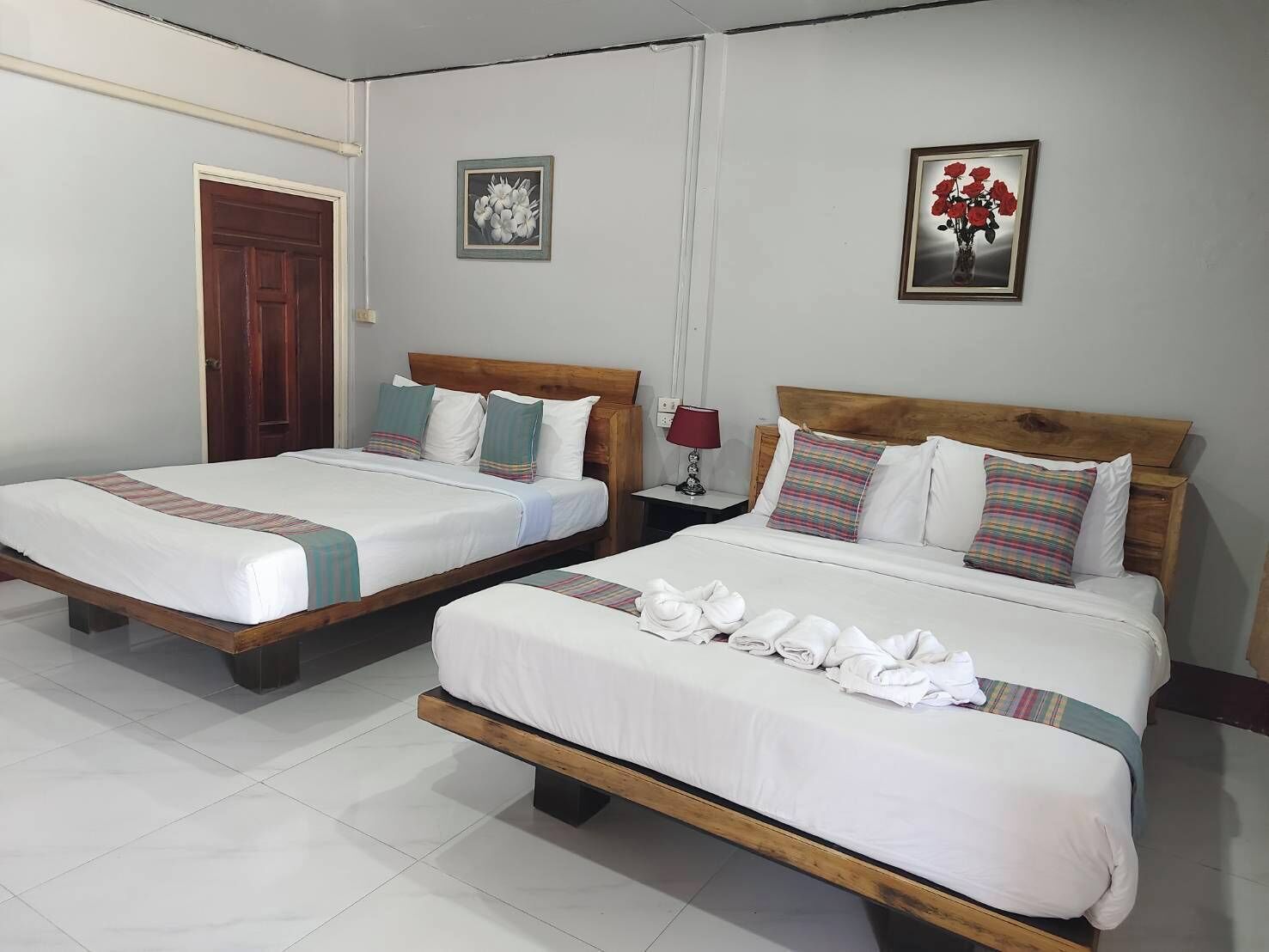 Dos camas individuales con estructura de madera y ropa de cama blanca, una puerta de madera y dos cuadros enmarcados en la pared.