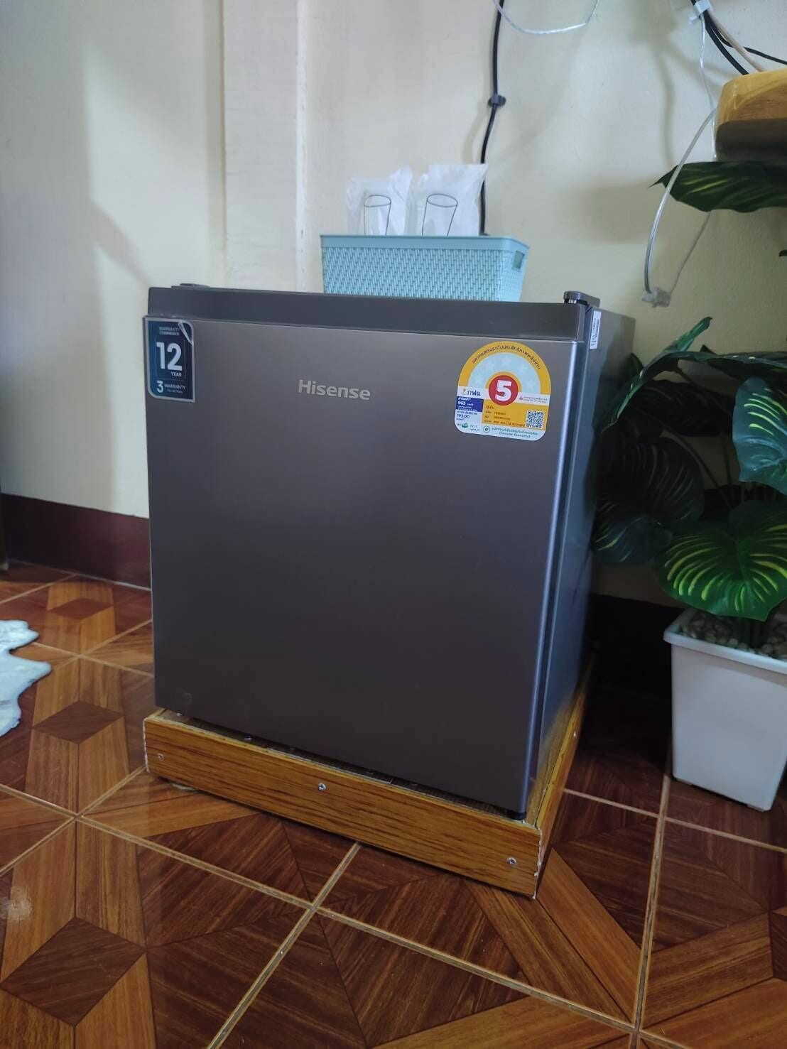 Un frigorifero Hisense compatto con adesivo che indica una garanzia di 12 anni, posizionato su una piattaforma di legno con piastrelle decorate.