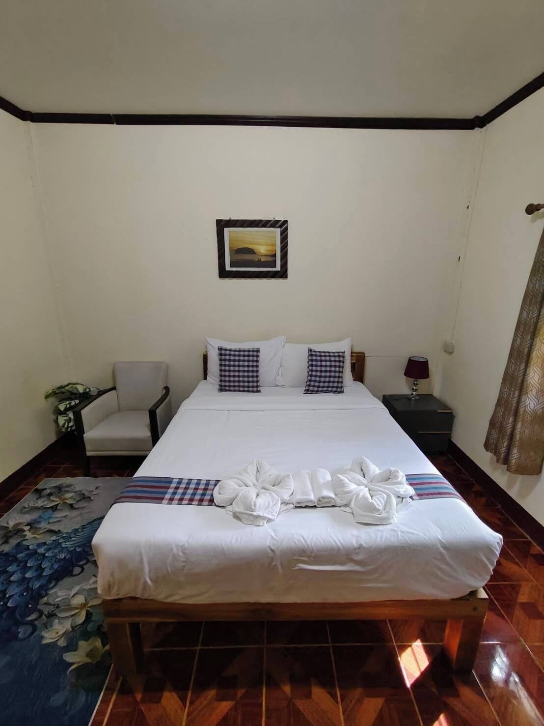 Una cama bien hecha con un cojín de cuadros, una mesita de noche con una lámpara y un cuadro en la pared.