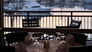 A dining table with chairs and wine glasses, set against a view of a marina with boats. - Modern Sandpiper Retreat: 2 King Suites + Resort Golf, Pickleball & Dining (Destin)