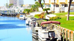 A marina with boats docked, a grassy area with palm trees, and a building with balconies in the background. - Modern Sandpiper Retreat: 2 King Suites + Resort Golf, Pickleball & Dining (Destin)