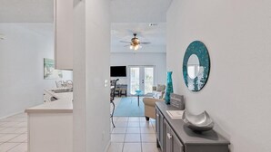 A modern kitchen with a white countertop, a ceiling fan, and a dining area with a glass table and chairs. - Modern Sandpiper Retreat: 2 King Suites + Resort Golf, Pickleball & Dining (Destin)
