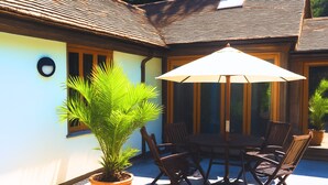 An outdoor patio with a table and chairs, a large umbrella, and a potted plant. - Dog Friendly Cottage with Outdoor Swimming Pool, Tennis & Table Tennis (Chichester)