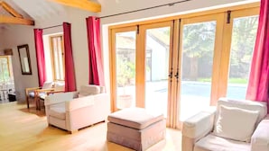 A spacious living area with a sofa, ottoman, and a dining table. - Dog Friendly Cottage with Outdoor Swimming Pool, Tennis & Table Tennis (Chichester)
