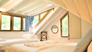 A bedroom with two beds, a window with curtains, a mirror, and a wooden beam structure. - Dog Friendly Cottage with Outdoor Swimming Pool, Tennis & Table Tennis (Chichester)