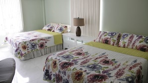 Habitación con dos camas, cada una con ropa de cama floral, una mesita de noche con lámpara y una ventana con persianas.