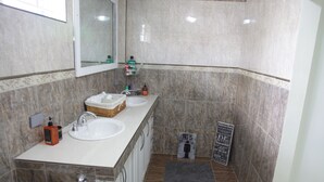 Un baño con dos lavamanos, un espejo, un perchero para toallas y un pequeño cartel.