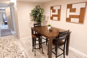 A dining area with a wooden table, four chairs, a potted plant, and two abstract wall art pieces.
