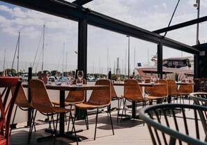 An outdoor dining area with tables and chairs, overlooking a marina with boats. - Rural Mezzanine Studio with Shared Swimming Pool, Tennis, Table Tennis & zip wire (Chichester)