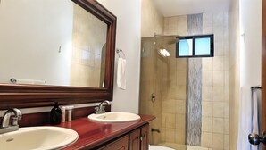A bathroom with a wooden vanity, two sinks, a large mirror, and a shower area with a glass door.
