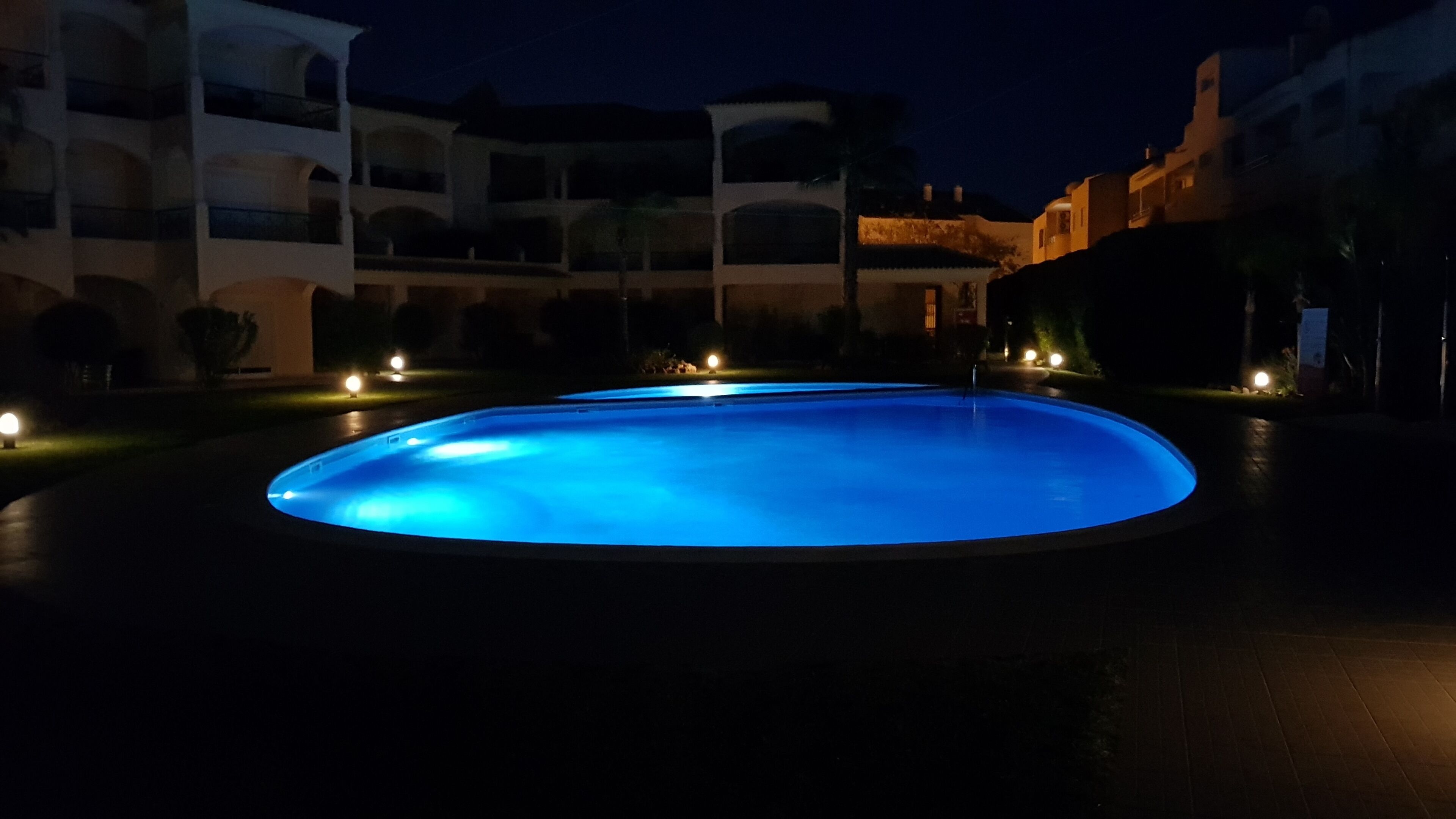 Una piscina por la noche con edificios aledaños.