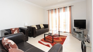 A modern living room with a black leather sofa, a glass coffee table, and a flat-screen TV. - Walk to beach/marina, pool view, aircon, wifi, parking. Ideal Families/Groups. (Vilamoura)